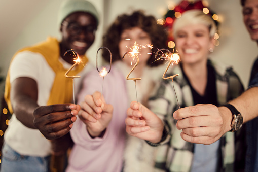 Portrait of a multi - ethnic group of young people lighting sprinklers and celebrating the New Year's eve at home.