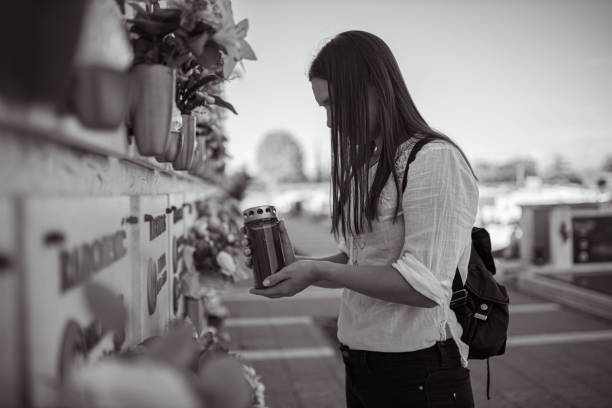 Woman at the cemetery missing the loved one Black and white photo of an sad young woman, grieving on the place of burial, and memorial cemetery, while holding an candle place of burial photos stock pictures, royalty-free photos & images