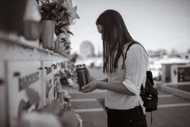 Black and white photo of an sad young woman, grieving on the place of burial, and memorial cemetery, while holding an candle