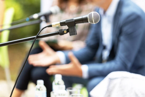 Round table event or business conference Microphone in focus against blurred people at round table event or business conference business conference stock pictures, royalty-free photos & images