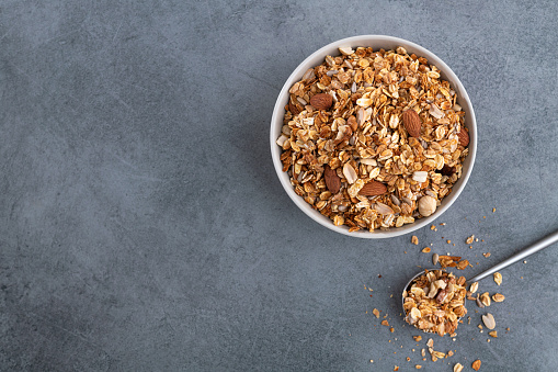 Fresh granola with almonds in a white bowl. Stone gray background. breakfast food. Top view.