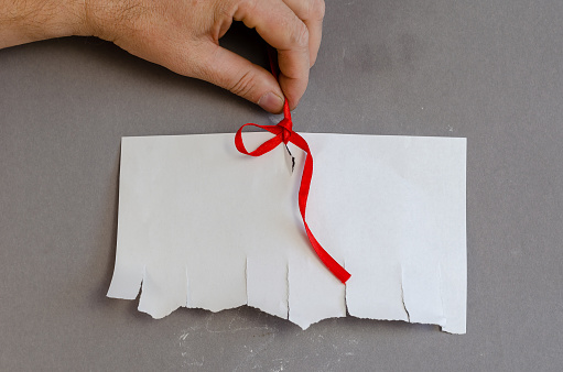 White sheet of paper with tear-off pieces and red ribbon against a gray background. The hand holds the Tied Blank Sheet of Ads vertically.