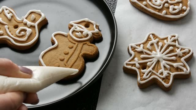 Decorating holiday gingerbread cookie. Pastry bag with white icing. Making handmade festive new cookies for gift in shape of snowman. Christmas and new year traditions