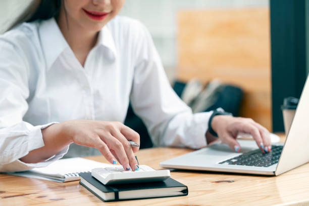 istock Cropped shot of woman hand using calculator and computer while sitting at the table in modern office room. 1345801556