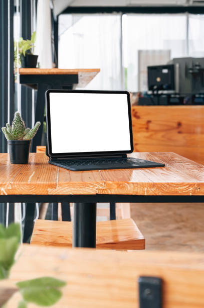 istock Mockup blank screen tablet with magic keyboard on wooden table in cafe room. Vertical view. 1345802294