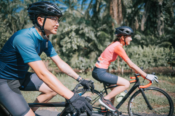 side view asian chinese couple cyclist enjoy road biking cycling during weekend morning together rural scene side view asian chinese couple cyclist enjoy road biking cycling during weekend morning together rural scene cycling vest photos stock pictures, royalty-free photos & images