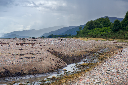 View from the beach of foreground stream and distant mountains on the shores of Loch Linnhe in Scotland..