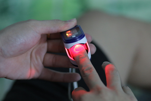 An Asian young man is using oximeter tracing pulse at home.