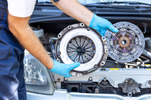 Automotive technician holding used car pressure plate and clutch disc in front of the vehicle engine stock photo