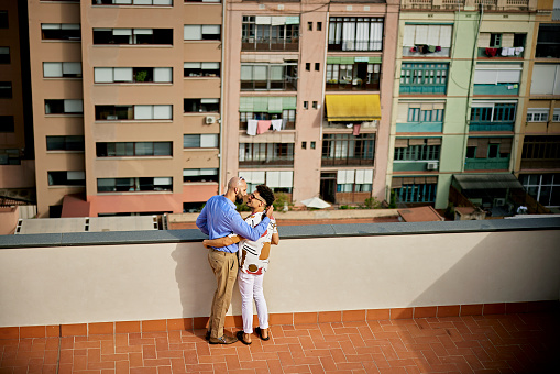 Elevated view of mid adult Brazilian men in smart casual attire standing face to face with arms around each other and enjoying a private moment.