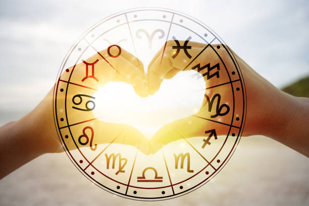 女性と男性の手は、手を通過する太陽の光が占星術のシンボルを持つ心臓の形です - 愛 ストックフォトと画像