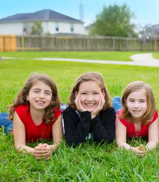 Children girls group lying on lawn grass smiling happy together in a row
