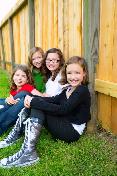Grils group in a row smiling sitting in a wooden fence outdoor