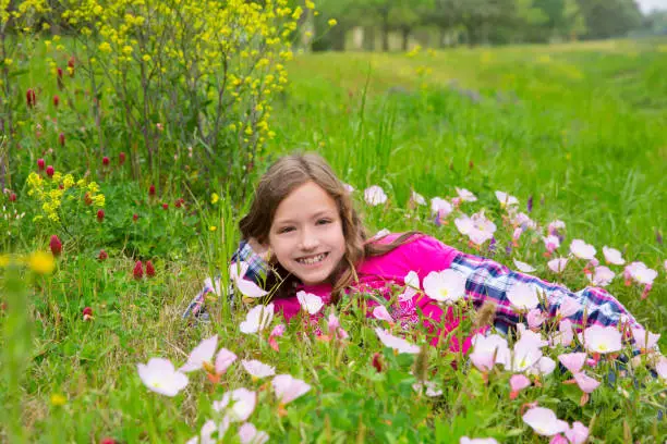 Happy relaxed kid girl smiling on a spring flowers meadow with green grass
