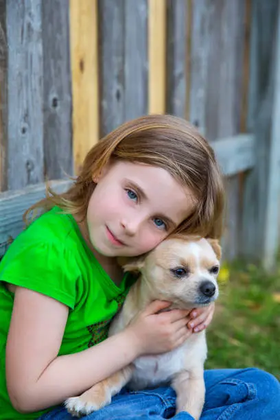 Blond happy girl with her chihuahua doggy portrait on backyard fence