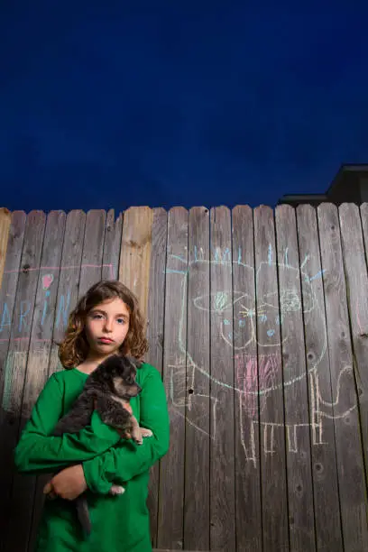 children girl holding puppy dog after chalk painting on backyard wood fence