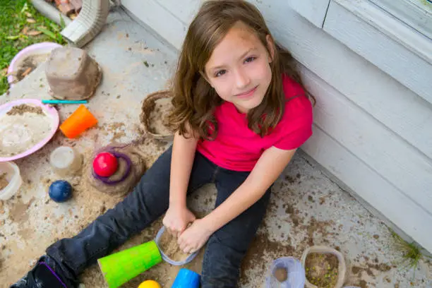 girl playing with mud in a messy soil smiling portrait looing from high point