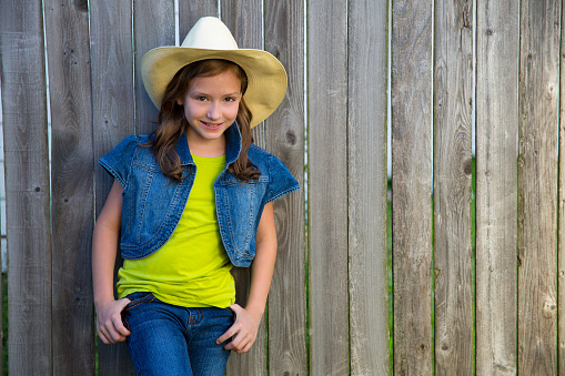 Children girl as kid cowboy girl cowgirl posing on wooden fence far west style