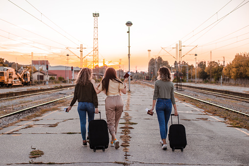 Tourist girls walking with suitcase, waiting for train on railway platform, enjoying weekend city break and susnet