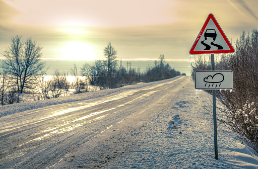 Winter, a road sign covered with ice warning of a slippery road