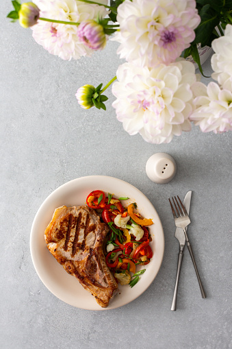 Delicious hearty dinner in plates on the table and a bouquet of beautiful autumn flowers, fried pork entrecote on the bone with stewed vegetables
