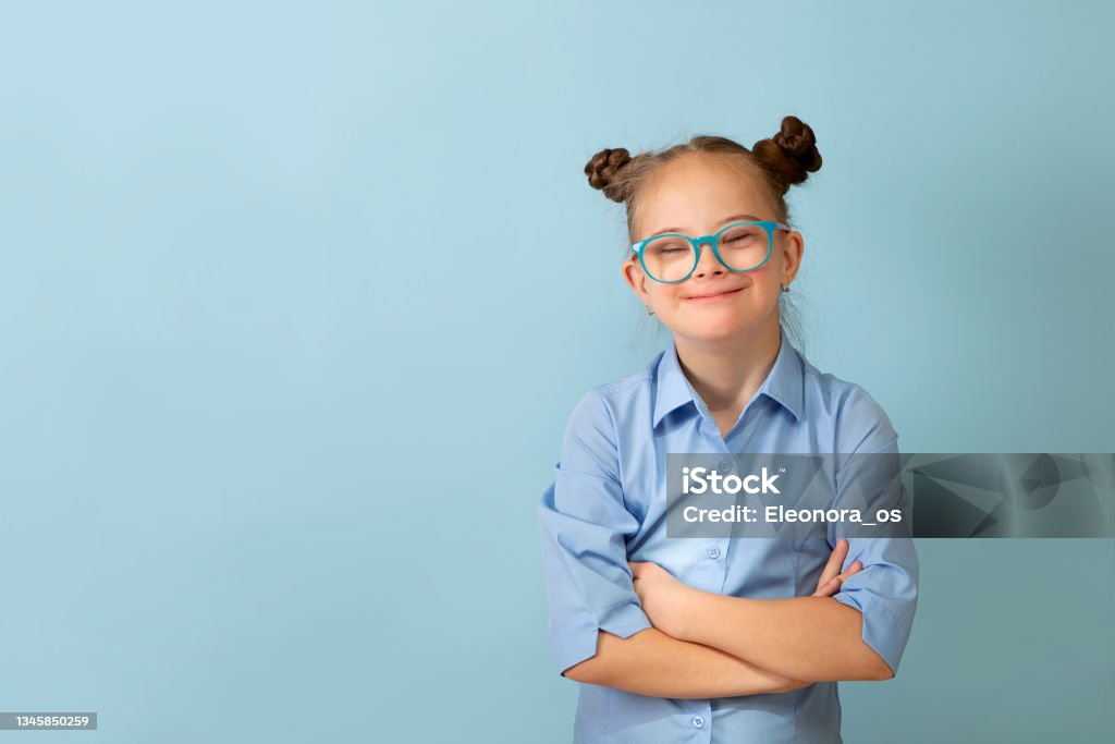Happy girl with Down syndrome having fun and laughing in the studio Happy girl with Down syndrome. Having fun, laughing. Funny pigtails. Studio. Portrait on a blue background Down Syndrome Stock Photo