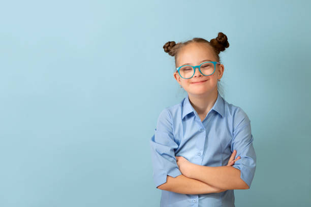 Happy girl with Down syndrome having fun and laughing in the studio Happy girl with Down syndrome. Having fun, laughing. Funny pigtails. Studio. Portrait on a blue background formal portrait photos stock pictures, royalty-free photos & images