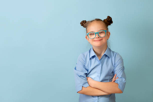 Happy girl with Down syndrome having fun and laughing in the studio Happy girl with Down syndrome. Having fun, laughing. Funny pigtails. Studio. Portrait on a blue background down syndrome stock pictures, royalty-free photos & images