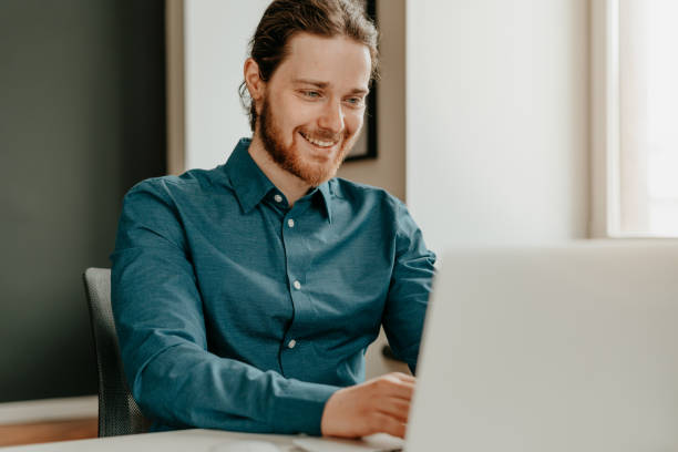 istock Smiling young male office worker typing on keyboard and looking at laptop screen in office. 1345852309
