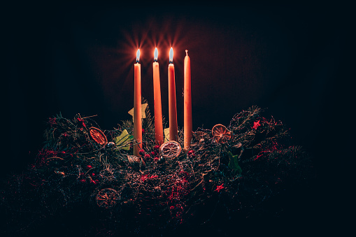 3 shining candles on colorful decorated advent wreath with four candles on black background