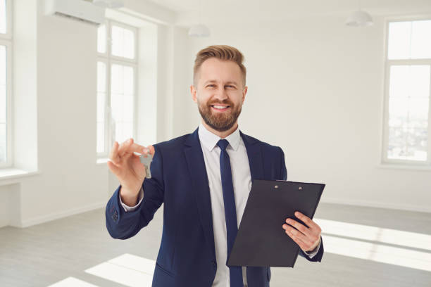 agente de negocios con llaves de un nuevo hogar sonriendo en el fondo de una nueva casa de apartamentos - real estate agent fotografías e imágenes de stock