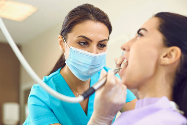 Serious dentist removing calculus from client's teeth with ultrasonic scaler in modern dental clinic stock photo