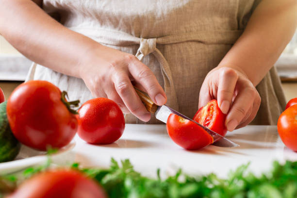 istock Chef slicing tomato using knife on the table in restaurant. Process of cutting and preparation food in kitchen. 1345861009