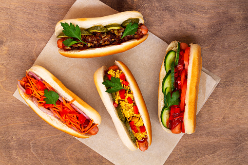 Homehand tasty Hot dogs with different toppings: pickles, fried onion, tomatoes and carrots with green on a wooden background with copy space. flat lay. Fast food concept top view.