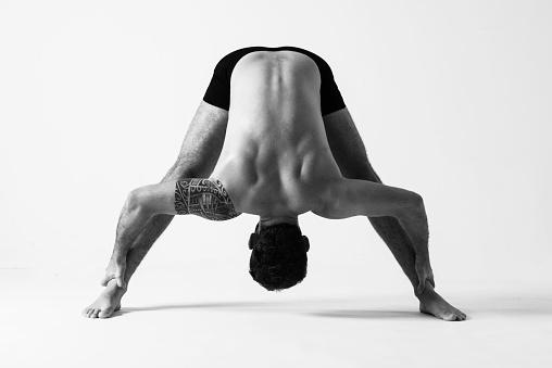 Young man practicing yoga. Bend pose, open wide, Prasarita Padottanasana.