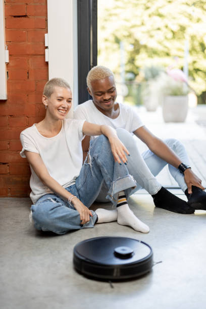 istock Couple sitting on floor with robot vacuum cleaner 1345862462