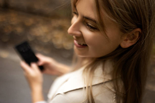 istock Smiling young woman in raincoat using smart phone 1345862687