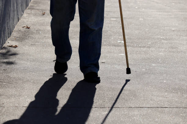 istock Man walking with a cane down the street, shadow on asphalt 1345863583