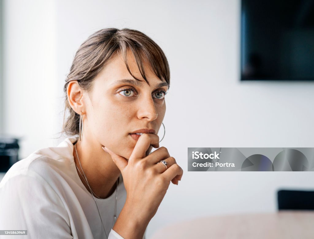 Young businesswoman listening in meeting Close-up of a young businesswoman listening in meeting. Female executive sitting with hand on chin paying attention on the conversation in meeting. Listening Stock Photo