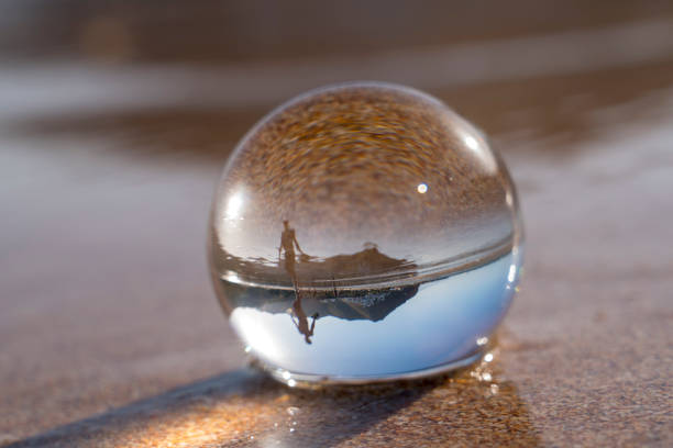 Crystal ball resting in wet sandy beach, red sand, reflecting a person, mountain and sky