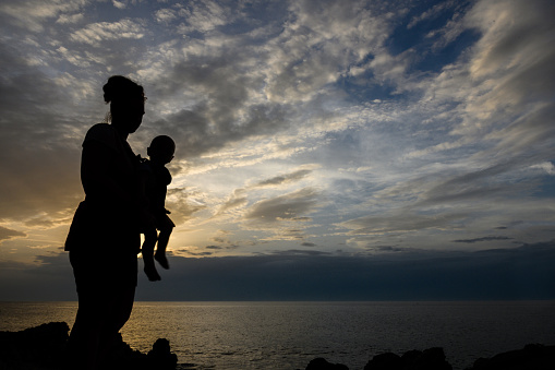Silhouette of mother holding a baby in a baby carrier while on the beach
