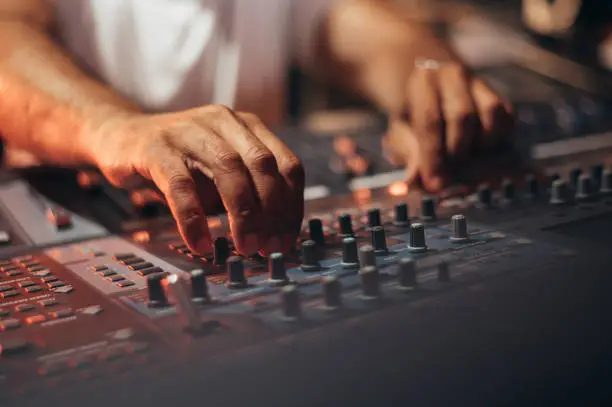 Music producer hands while working on a mixing soundboard while in his studio