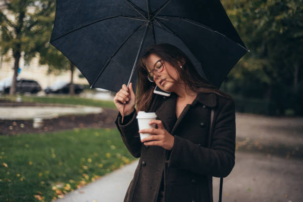istock Beautiful young woman using smartphone and holding an umbrella 1345867844