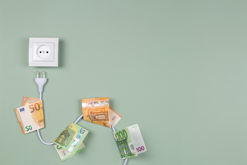 Electric power plug with euro banknotes on it and electric socket on light green background. Electricity cost and expensive energy concept.