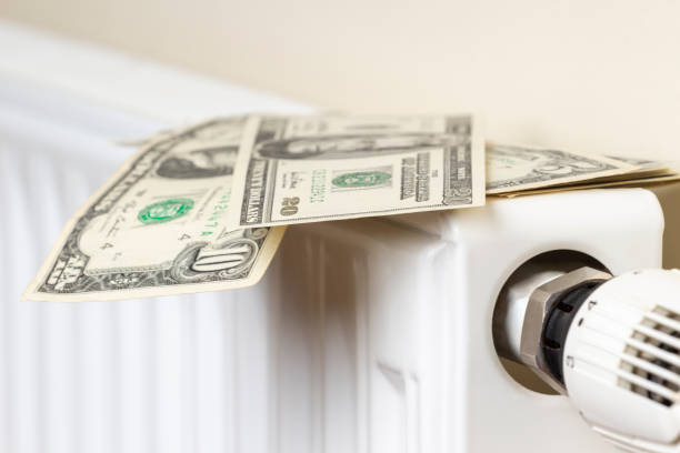 istock Expensive heating costs. Paying bills. US dollars banknotes on heating radiator battery with temperature regulator at home 1345871151