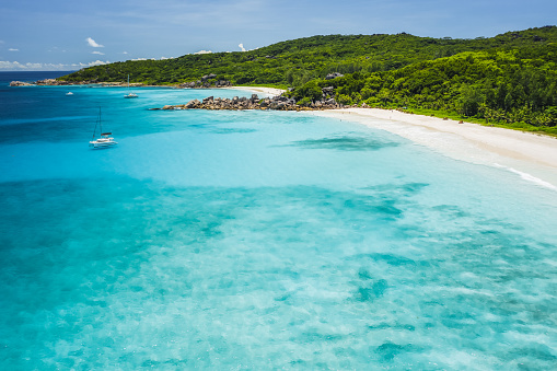 Aerial drone view of tropical paradise like beach with pure crystal clear turquoise water, bizarre granite rocks and coconut palm trees. Travel concept.