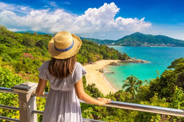 Woman traveler wearing blue dress and straw hat at  Panoramic aerial view of Laem Sing beach on Phuket island, Thailand in a sunny day