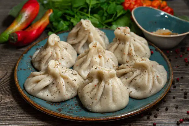 Photo of Georgian-style khinkali with meat on a handmade ceramic plate. Sprinkled with ground pepper.