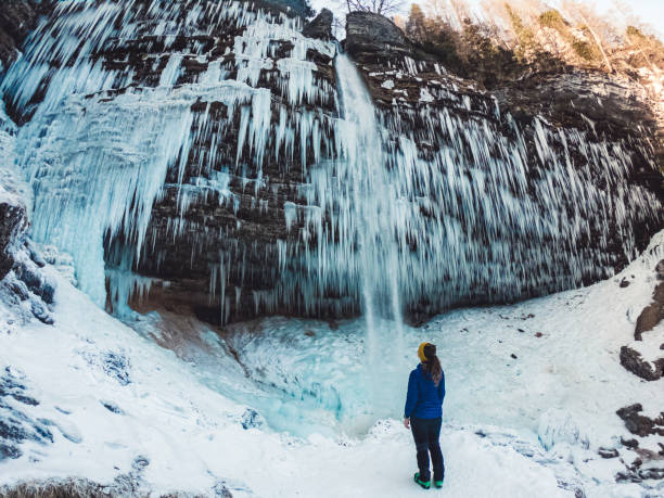 istock Frozen winter waterfall with icicles and female hiker standing underneath 1345890710