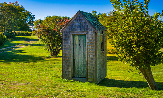 A weathered outhouse by the side of a rural  unpaved road on Cape Cod